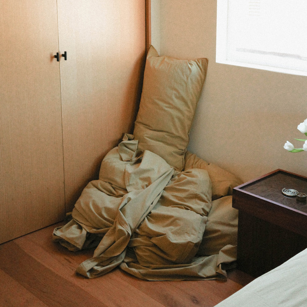 Green sheets and pillowcase stacked in the corner of a minimalist room 