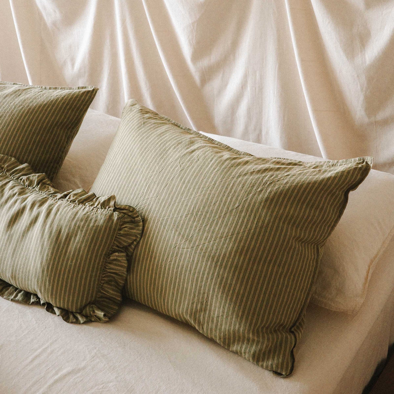 Close up on striped green pillows against a cream colored bed and fabric head board