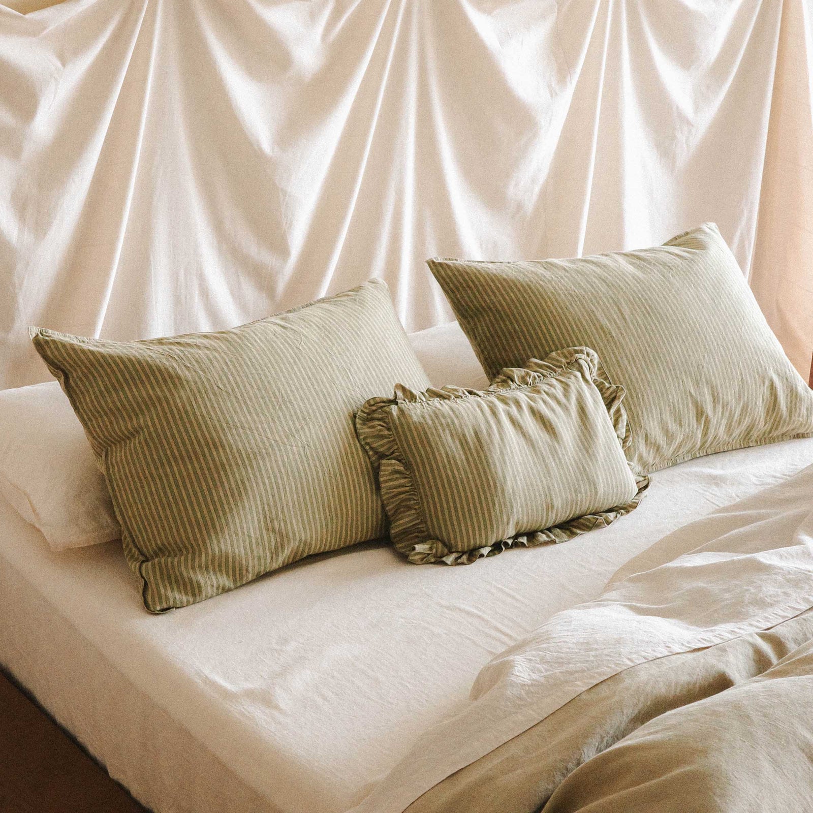 Top half of a bed in a bright bedroom setting. On the bed are three stripe green pillows and one is a mini ruffle