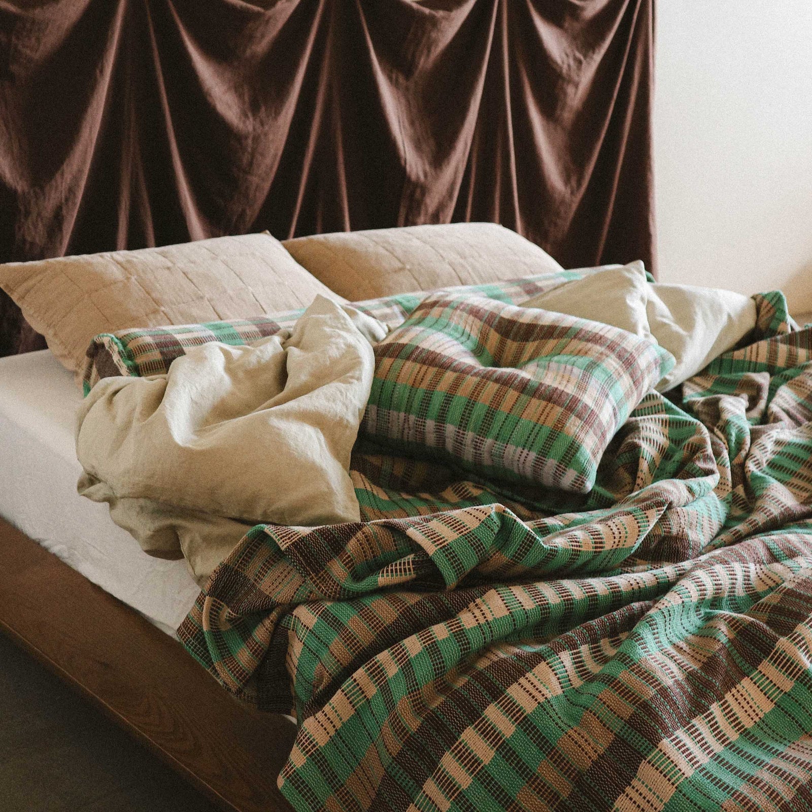 A close up of a slept in bed with the Yara bedcover and the Yara throw pillow and Yara bolster paired with cream colored sheets