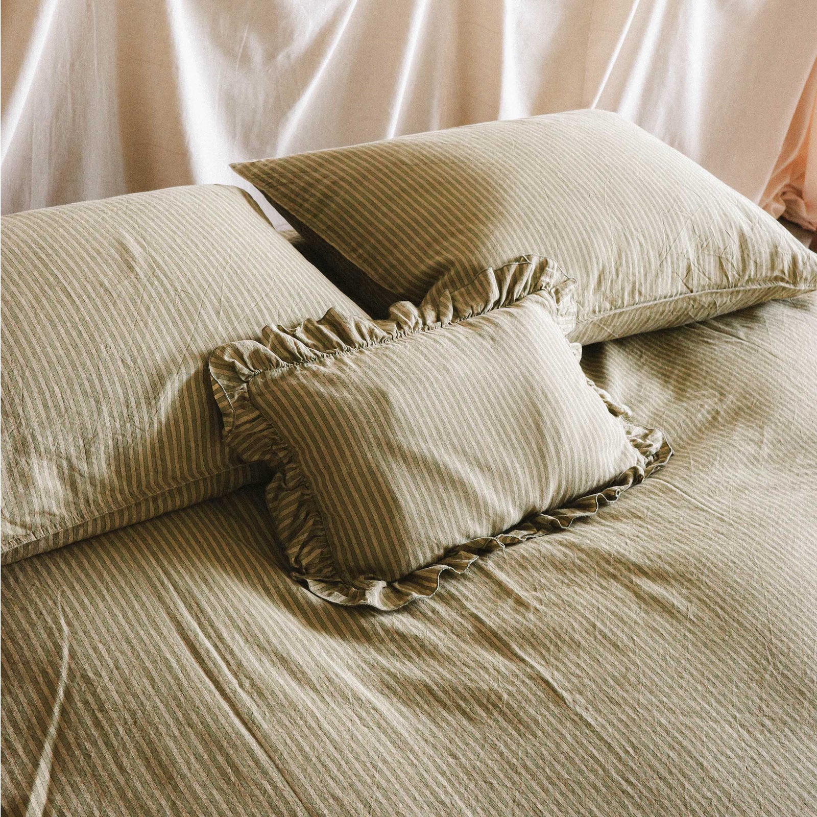 Close up of the top half of a bed with stripped green sheets and a mini ruffle pillow in a bright bedroom setting