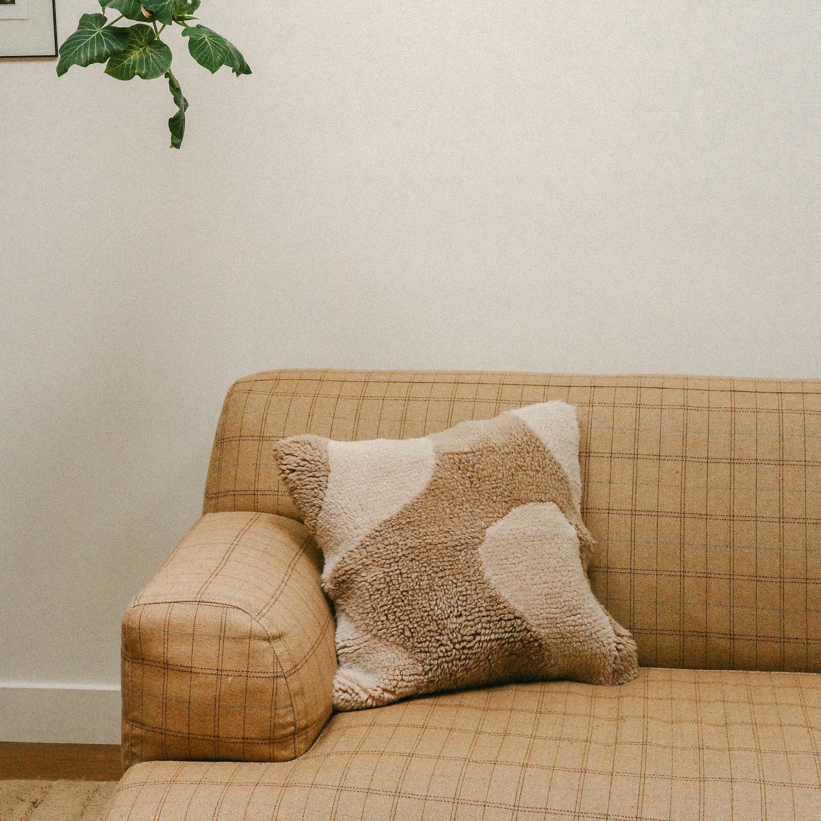 A living room setting with a checkered tan sofa with the Otis pillow resting. The Otis is a square throw pillow with an organic design in cream and beige.