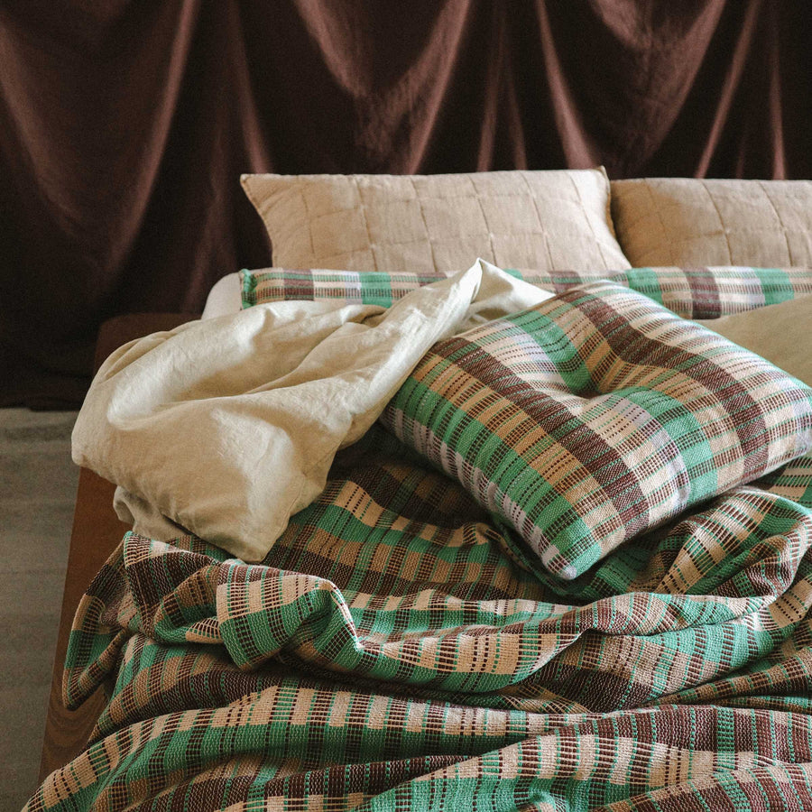 A lived in bed with a casually crumpled Yara bed cover and Yara throw pillow resting on top