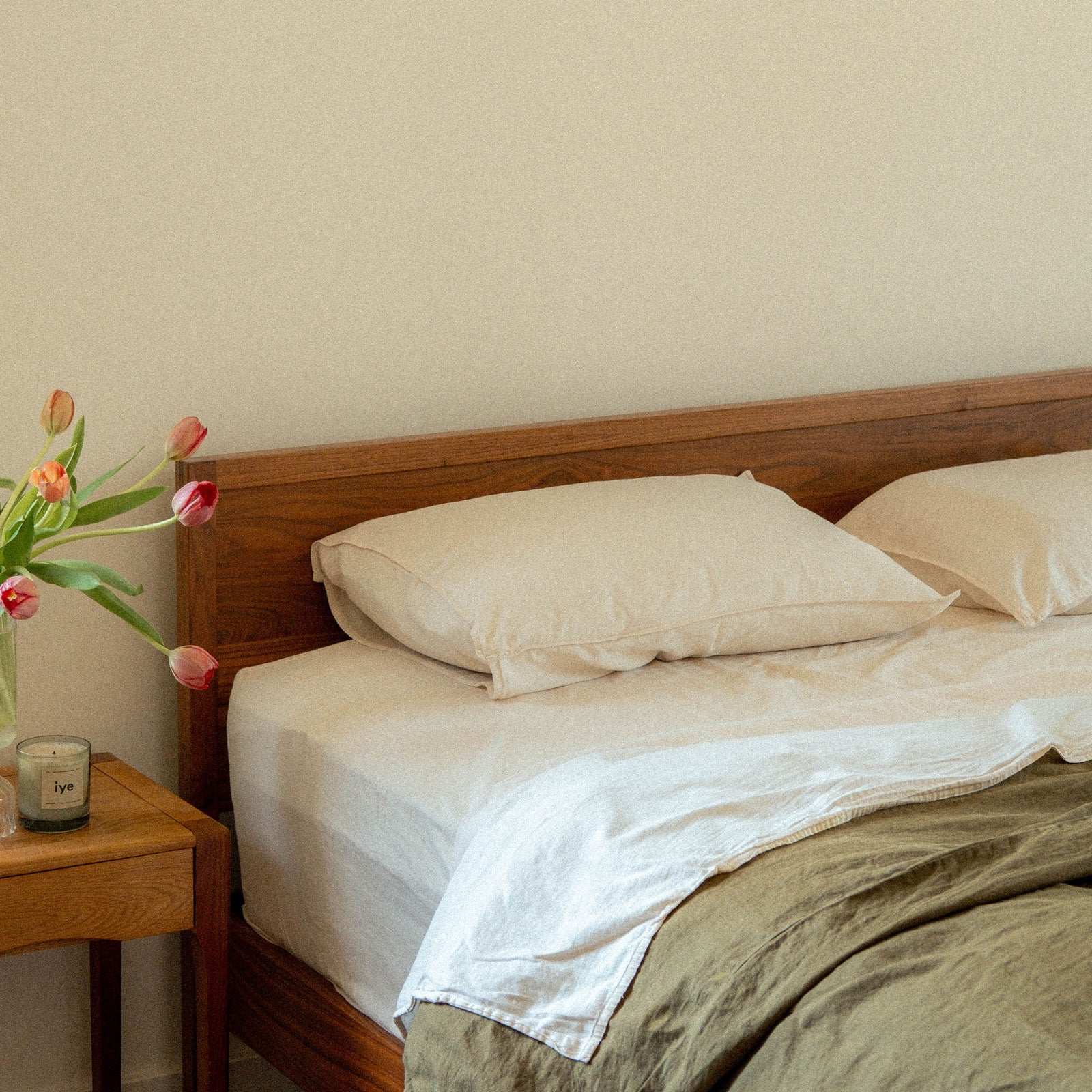 A bed with two Oat pillows and sheets with a green duvet cover in a bedroom setting 