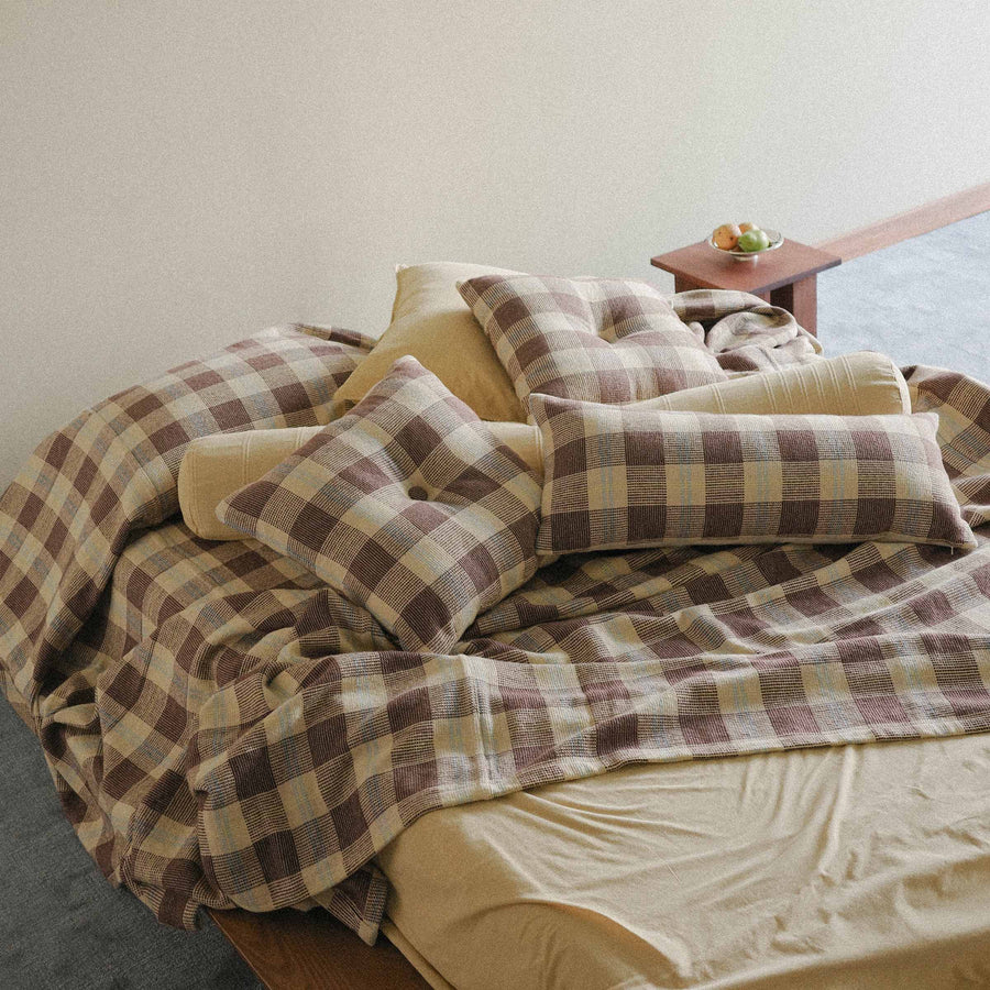 A bed with Pillows, brown and yellow checkered and yellow in a bright bedroom