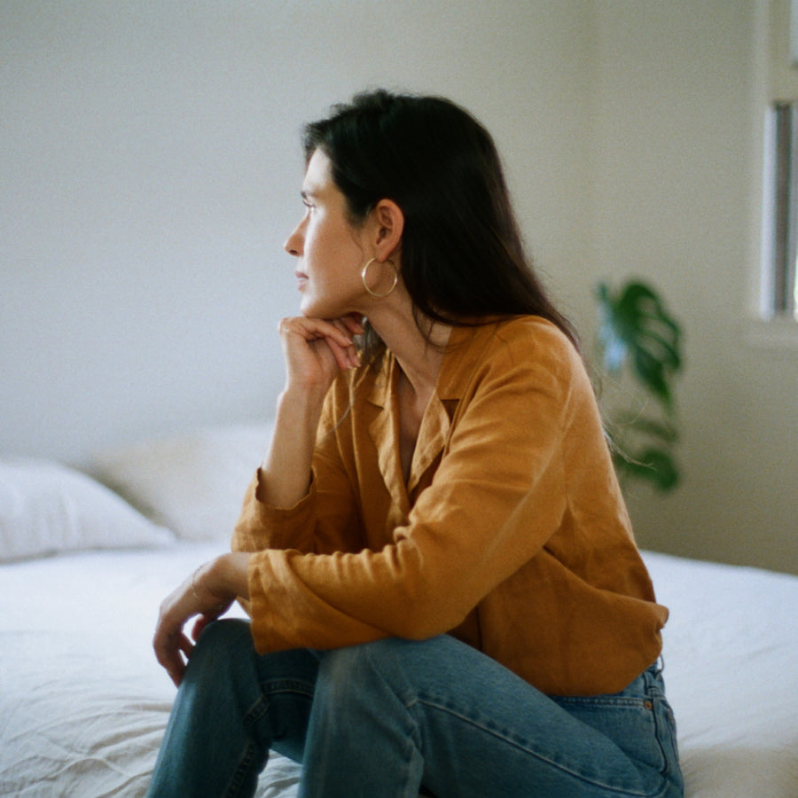 A woman sits on a white bed looking off to the left