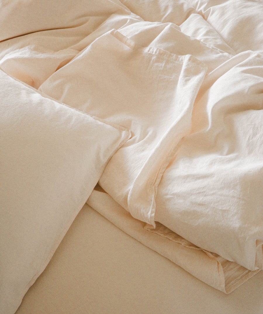 Close-up of soft off-white bedding with rumpled sheets and pillows, showing a warm cream or ivory tone.