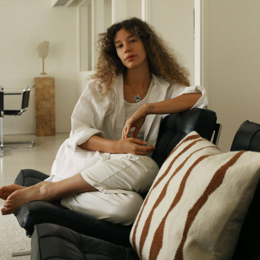 A woman with curly hair sits on a black leather sofa. A striped cream and brown throw pillow rests on the sofa in the foreground, with a modern, minimalist room in the background.