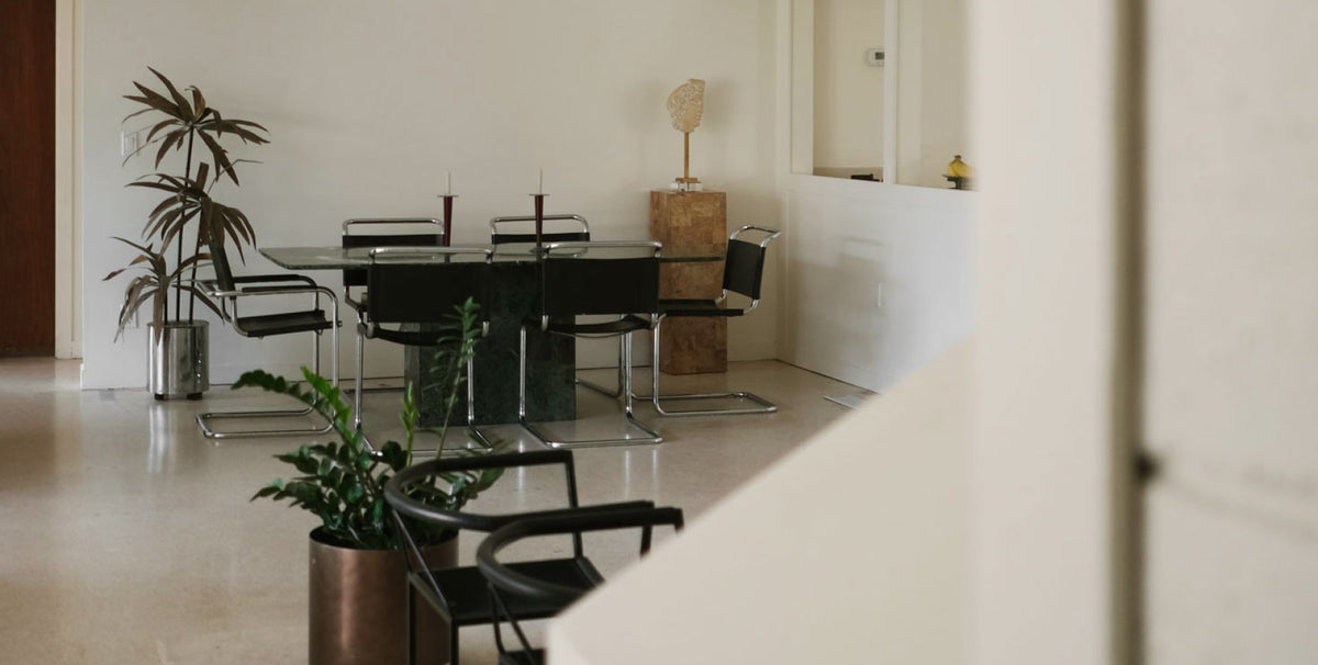 Mid century modern dining room with a glass table, black chairs and tall i ndoor plants