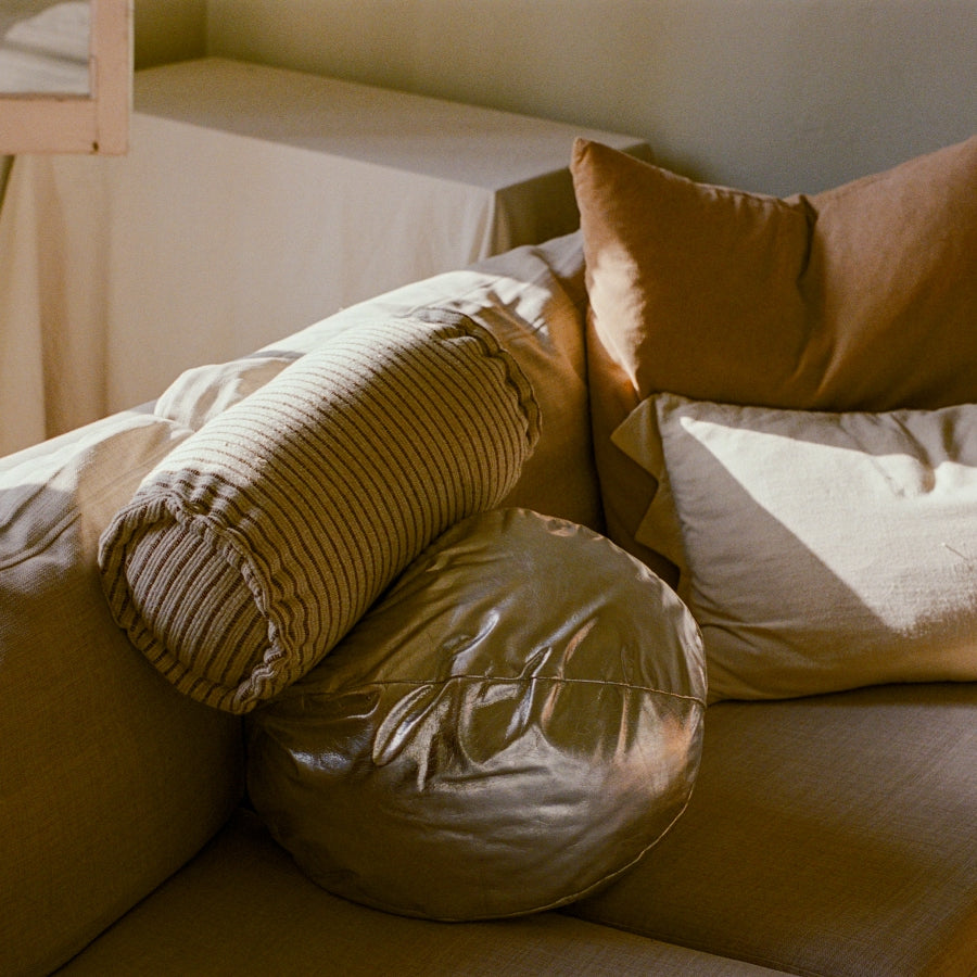 A cozy arrangement of home decor pillows on a sofa, including a ribbed cylindrical lumbar pillow, a round bolster pillow, and solid-colored accent pillows in warm beige and brown tones.