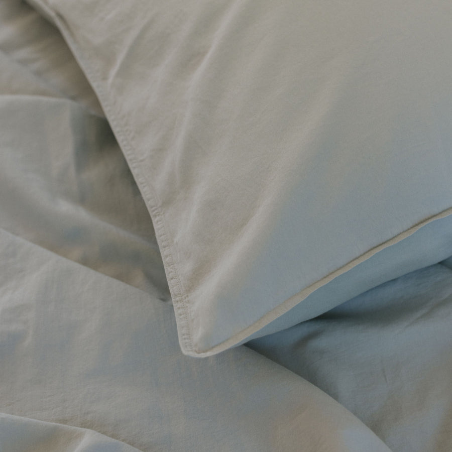 Close-up of light blue bedding, showing a folded pillowcase and matching duvet or sheet fabric with soft folds and a subtle sheen.