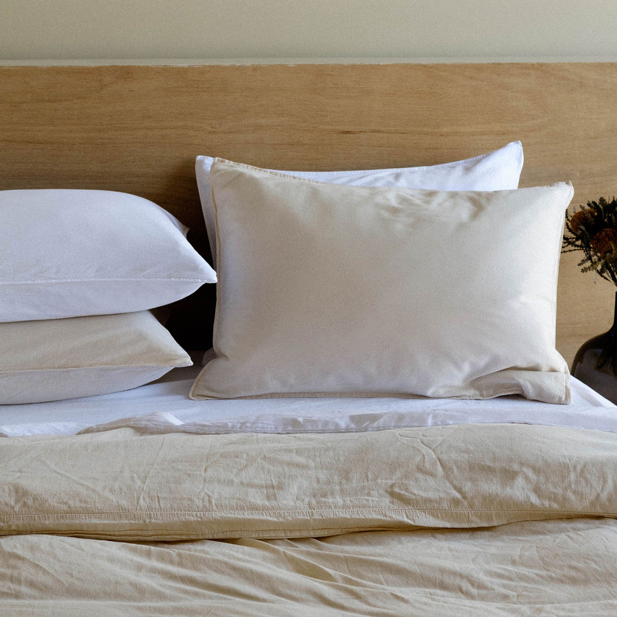 A bed made of oat and beige sheets against a wood headboard