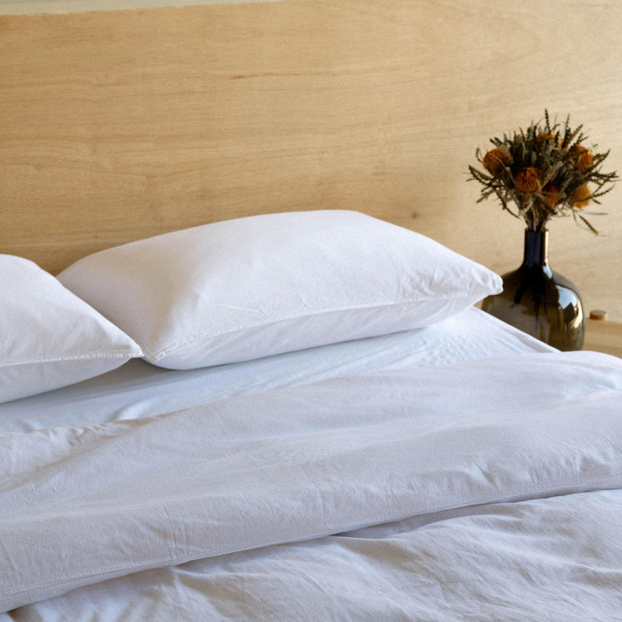 Close up of a bed dressed with matte sateen sheets in white against a wooden headboard